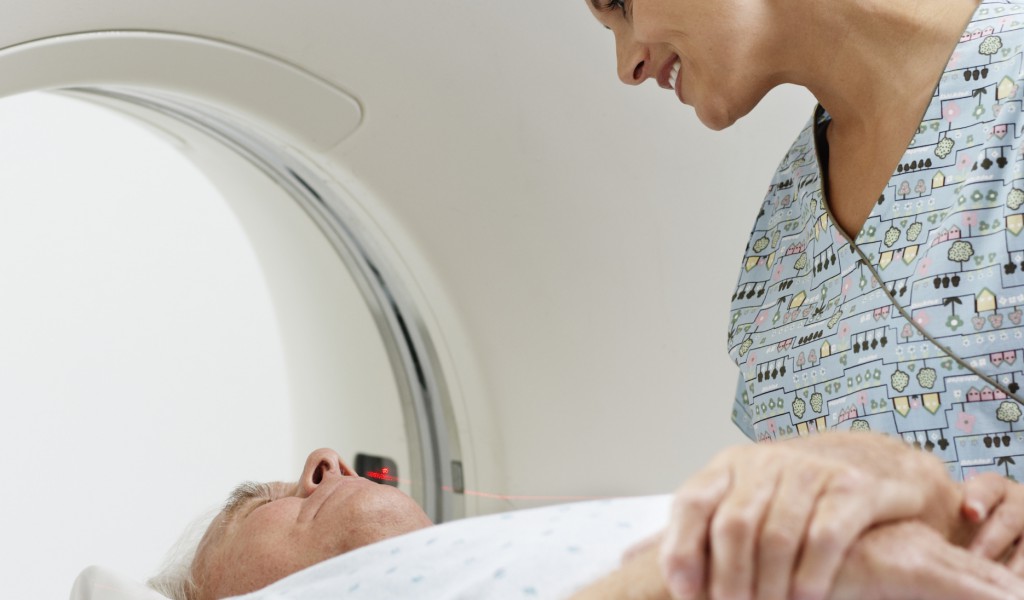 A female nurse comforts a male patient directly before undergoing a CT scan for liver assessment.
