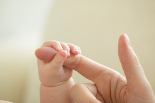 A baby with infant jaundice wraps finger around her mother's finger.